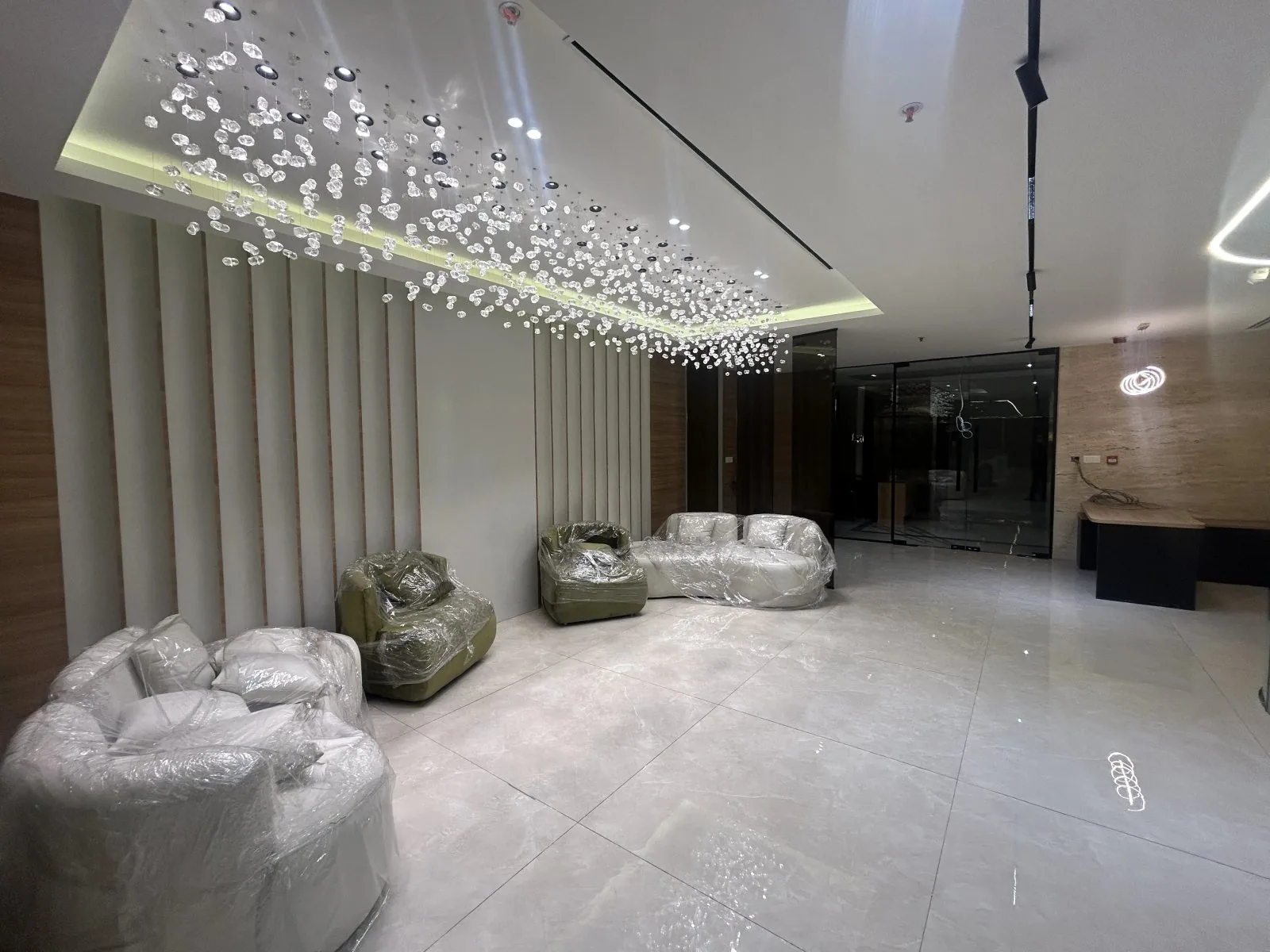Office reception lounge with a crystal-glass ceiling installation, slatted feature wall and marble-look floor tiles