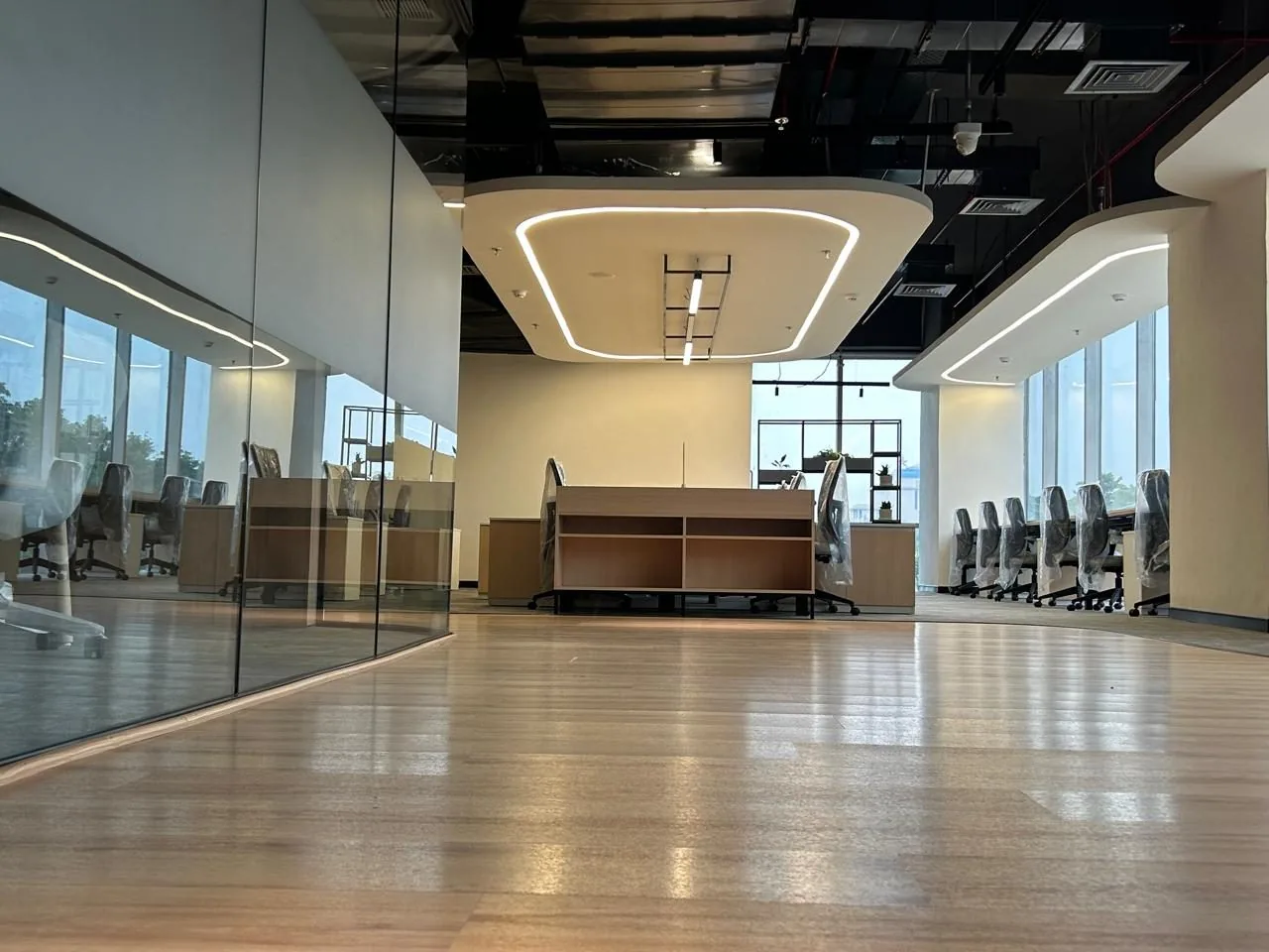 Open workspace seen through a glass partition, with a sculpted ceiling and seating along the window line